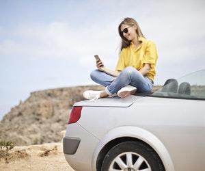 A young female looking at phone while sitting on a car